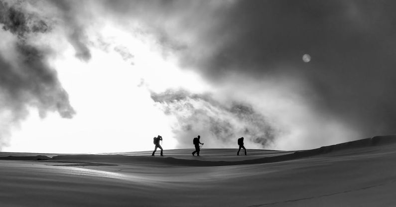Ski Trip - Black and white silhouettes of skiers and hikers crossing spacious snowy terrain under cloudy sky on cold winter weather